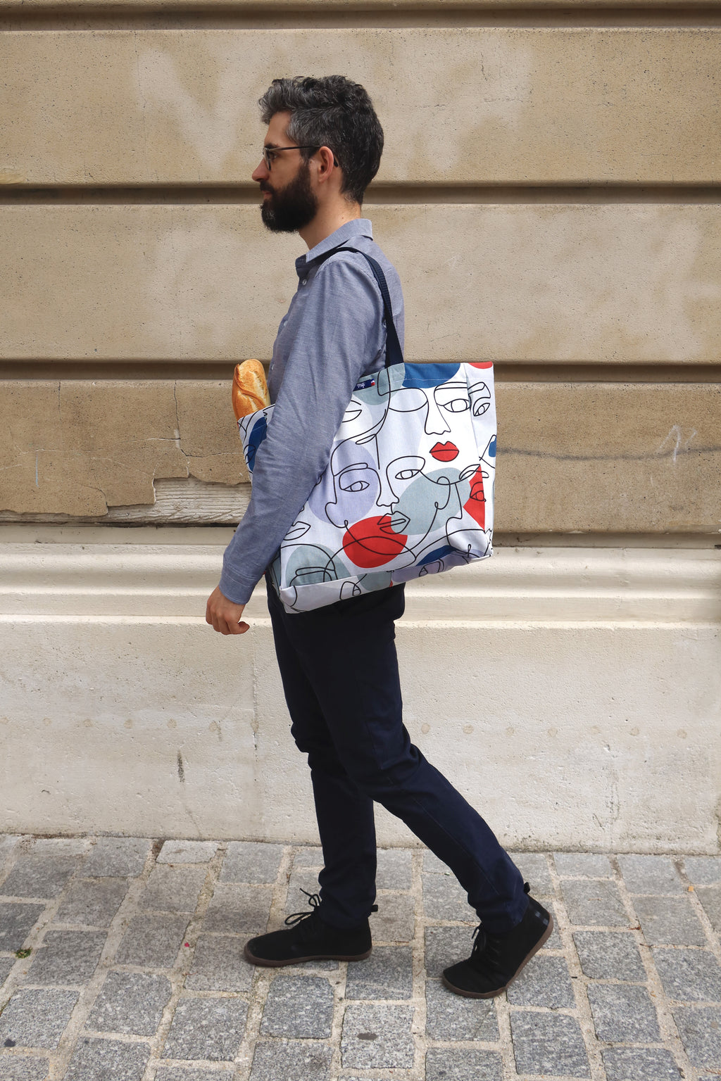 Photo du sac visages XL à l'epaule sur un homme dans la rue avec une baguette